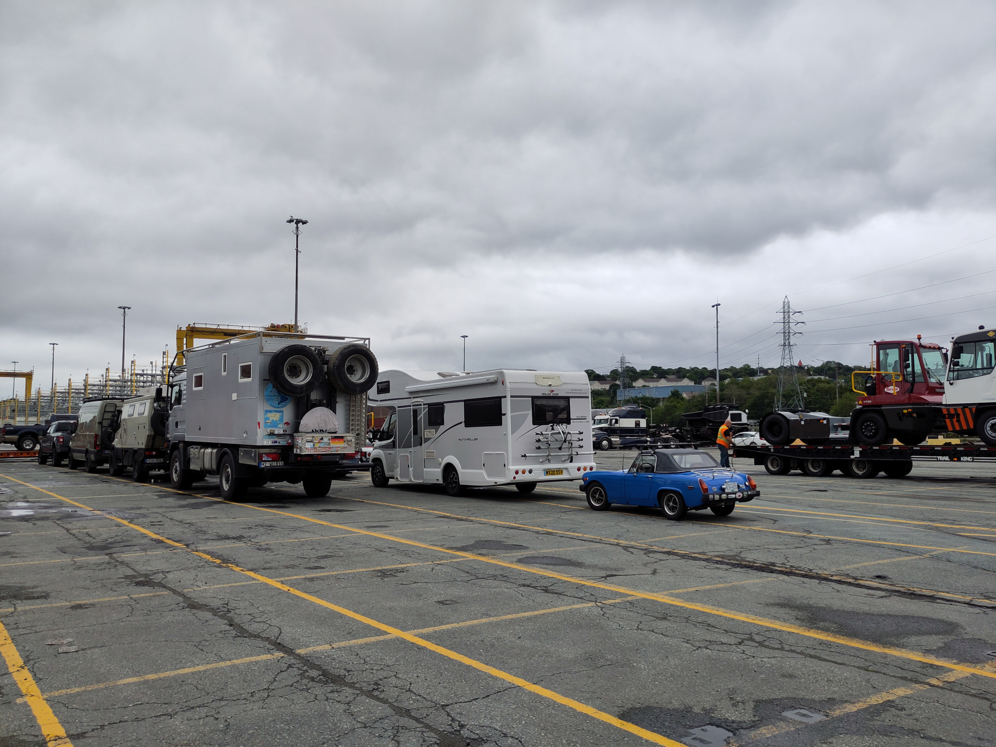 A small blue car in line to be loaded onto a ship. It is sitting behind some RVs.