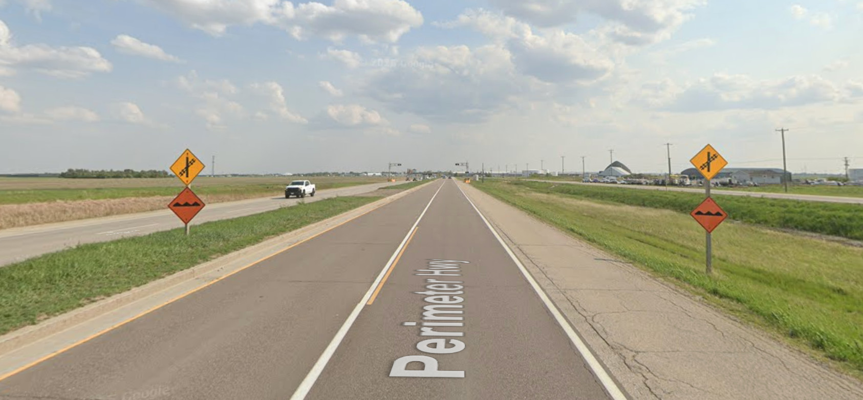 Screenshot of Google Street View from a highway in the prairies of Canada. There are signs for a railroad grade crossing on either side.